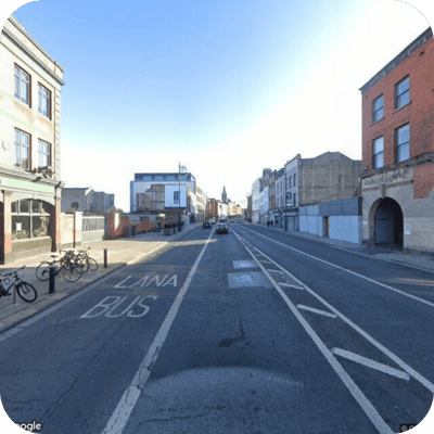 Street view of Thomas Street, Dublin, with bike lanes, parked bicycles, and buildings on either side. The road markings indicate a bus lane, and a few cars are visible in the distance.